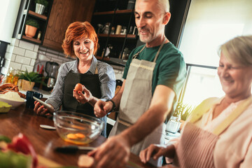 Group of senior friends at dinner party at home, cooking.