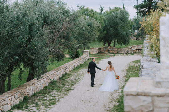 Happy stylish smiling couple walking in Tuscany, Italy on their wedding day. The bride and groom walk down the street by the hands. A stylish young couple walks. Husband and wife communicate nicely
