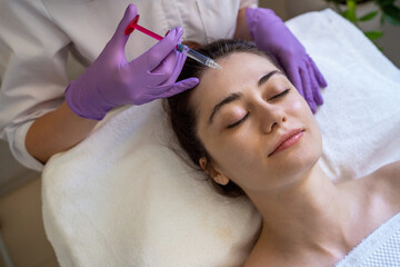 Top view of a woman receiving rejuvenation injection in face, anti aging non surgical cosmetic procedure in beauty salon. Beautician specialist hands in gloves