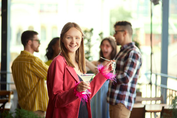 Happy, smiling, young woman in stylish clothes meeting with friends at cafe, having joyful time. Blurred people on background. Concept of friendship, meeting, party, communication, alcohol drinks