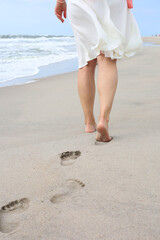 Beach trip - a woman walks along a sandy beach in a relaxed way, leaving footprints in the sand. Close-up of women's feet and shins on golden sand.