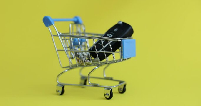 Woman hand puts car keys in toy shopping cart on yellow background. Buying expensive vehicles in car dealership concept. Transport advertising slow motion