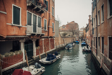 A charming Venice canal lined with parked boats, flanked by vibrant orange buildings.