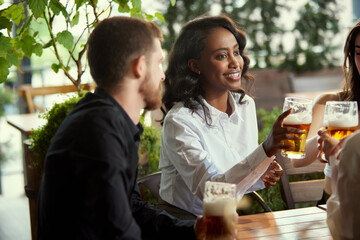 Positive, young people, colleagues, employees meeting at pub, cafe after work, drinking beer, relaxing and talking. Concept of leisure time, business, communication, fun, alcohol drink