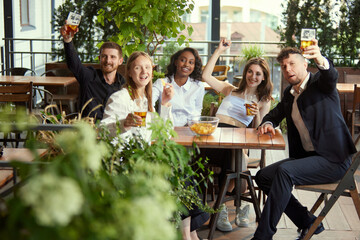 Beautiful, cheerful young people, colleagues, business people meeting after work at restaurant, pub, cafe. Good time. Concept of leisure time, business, communication, fun, alcohol drink