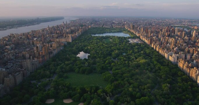 New York Cityscape at Sunset. Aerial Footage from a Helicopter. Modern Skyscraper Buildings Around Central Park in Manhattan Island. Focus on Nature, Trees and Lakes in the Park in the City