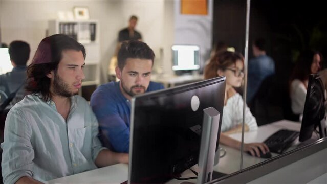 Coworkers looking at a computer and talking about work. Team of colleagues brainstorming together while working on the computer. Men colleagues discuss online project look at pc screen