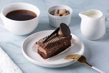 Delicious chocolate cake on plate and coffee on light table