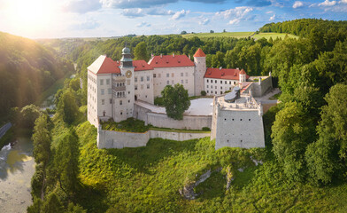 Traveling Poland castle concept: Panoramic Aerial view of Pieskowa Skała Renaissance castle, standing on Little Dog's Rock  limestone cliff in the green forest valley of river Prądnik. Summer, sunset. © Martin Mecnarowski
