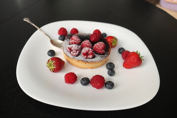 cream cake with raspberries and blueberries and small macaroons served on a large white plate