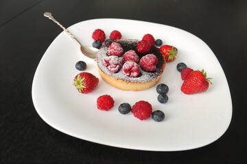 cream cake with raspberries and blueberries and small macaroons served on a large white plate
