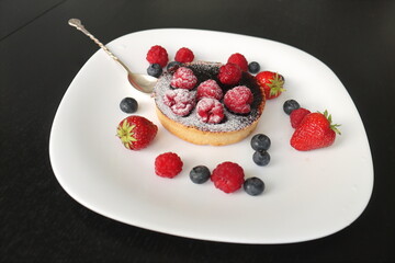 cream cake with raspberries and blueberries and small macaroons served on a large white plate