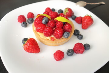 cream cake with raspberries and blueberries and small macaroons served on a large white plate