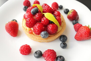 cream cake with raspberries and blueberries and small macaroons served on a large white plate