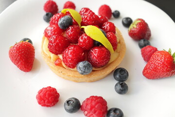 cream cake with raspberries and blueberries and small macaroons served on a large white plate