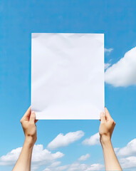 hands are holding a blank sheet of paper with realistic blue skies background - 624348613