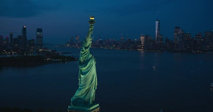 Aerial Helicopter Cinematic View of the Statue of Liberty with Manhattan Skyline Cityscape in the Evening. Panoramic View of New York City Skyscrapers and Jersey City Buildings at Sunset