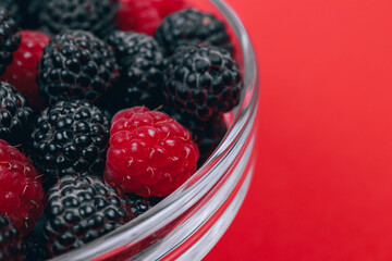 Close-up of glass bowl with red and black raspberries on red background. Macro shot.