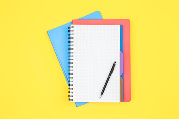 Notebooks and pen on a yellow background, top view.