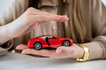  woman holding hand above toy red car as insurance.