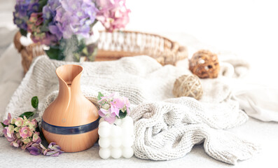 Aroma oil diffuser lamp, flowers and knitted element on a blurred background.