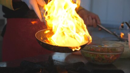 Detail view on flaming skillets in hand of professional chef. Male cook tossing and frying vegetables cooking tasty flambe style dish for visitors of restaurant. Concept of cooking. Slow mo Side view