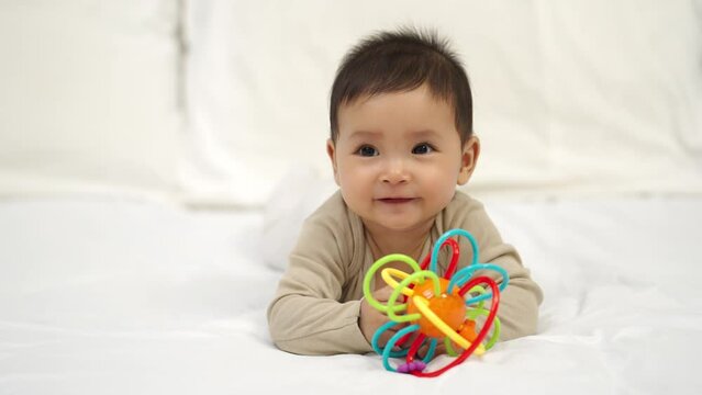 infant baby playing with colorful rubber bites toy on a bed
