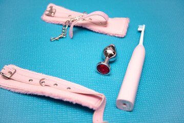 Sex toys on a blue background. Anal plug with pink handcuffs and electric toothbrush. Household appliances for sex. Sex concept.
