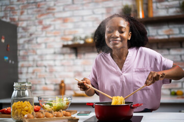 Young woman in kitchen. Beautiful African woman cooking pasta..