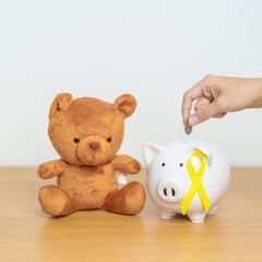 International Childhood Cancer Awareness month, Children toy with golden yellow color Ribbon with Piggy Bank for Donation, Charity, Campaign, Money Saving, Fund and World cancer day concept