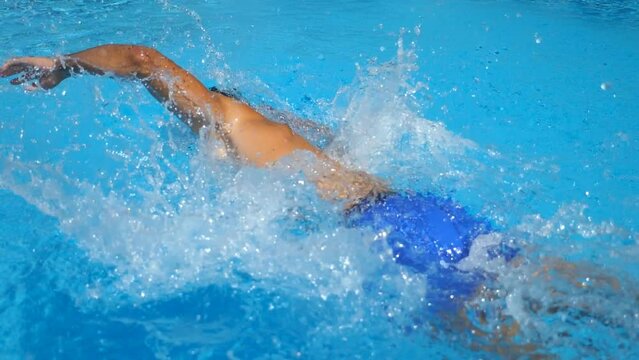 Young sporty guy floating in empty pool with clear blue water. Unrecognizable tanned man swimming and enjoying recreation on resort in sunny day. Male tourist refreshing in basin. Slow mo Back view