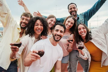 Fototapeten Group of young adult best friends having fun toasting a red wine glasses at rooftop reunion or birthday party, drinking alcohol. Happy people enjoying on a social gathering celebrating together. High © Jose Calsina