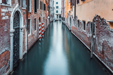 Fototapeta na wymiar Narrow water canal and red brick worn out buidings built on water in Venice, Italy. Long exposure photography.