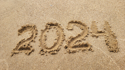 The numbers 2024 are written on the sandy beach. The concept of the new year