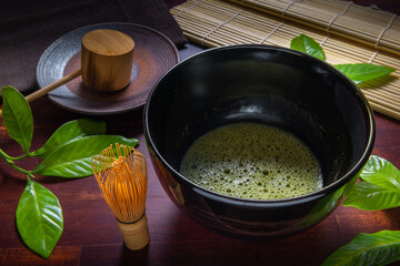matcha green tea and leaf in black bowl chawan decorated  Chasen, a bamboo matcha whisk, mat over wooden table, concept  of Japanese tea ceremony