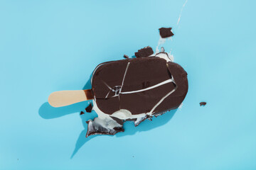 dropped upside down covered chocolate popsicle  with melting ice cream and hard shadow on blue background, minimalist summer food concept