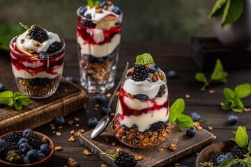 Homemade granola with greek yogurt, berries jam and fresh blackberries and blueberries in glasses