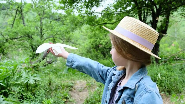 A girl in a hat launches a paper bird into the air in nature.