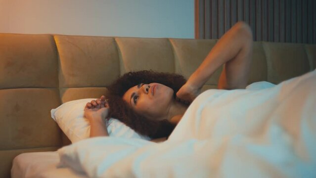 Troubled African American woman feeling neck pain, lying on uncomfortable pillow