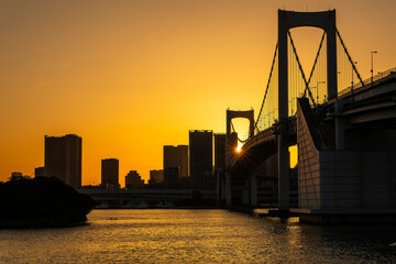 Obraz premium Orange sky as the sun sets behind the Rainbow Bridge and the Japanese capital city, Tokyo