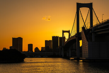 Obraz premium Orange sky as the sun sets behind the Rainbow Bridge and the Japanese capital city, Tokyo