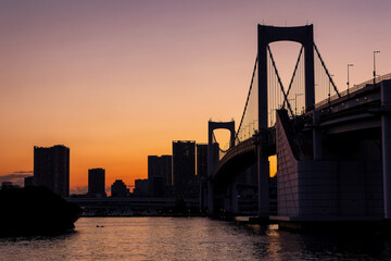 Purple and orange sky during sunset behind the skyscrapers of Tokyo and the Rainbow Bridge in Tokyo...