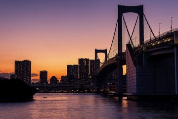 Obraz premium Purple and orange sky during sunset behind the skyscrapers of Tokyo and the Rainbow Bridge in Tokyo Bay