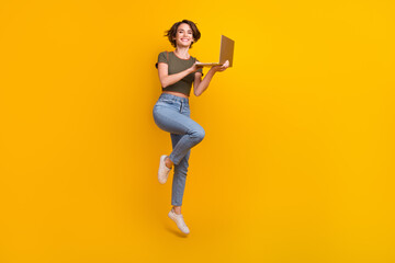 Full length photo of shiny adorable lady wear khaki t-shirt jumping communicating modern device isolated yellow color background