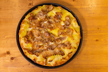 Pizza tonda di una rosticceria da asporto cotta nel ruoto e condita con porchetta, mozzarella e patate