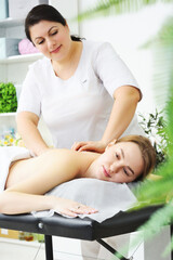 Obraz na płótnie Canvas masseur massages the back, lower back, shoulders and neck of a young woman against the background of a bright office and greenery.