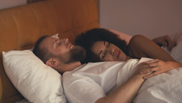 Happy interracial couple in love peacefully sleeping in bed and hugging, relax