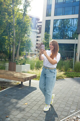 Cheerful young woman using her phone in the sunny city street. High quality photo