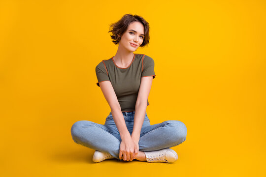 Full length photo of shiny charming girl dressed khaki top sitting floor legs crossed isolated yellow color background