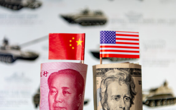 A roll of USD and Chinese Yuan with each country's national flags in front of a military background. A military spending, competition, arms race concept.